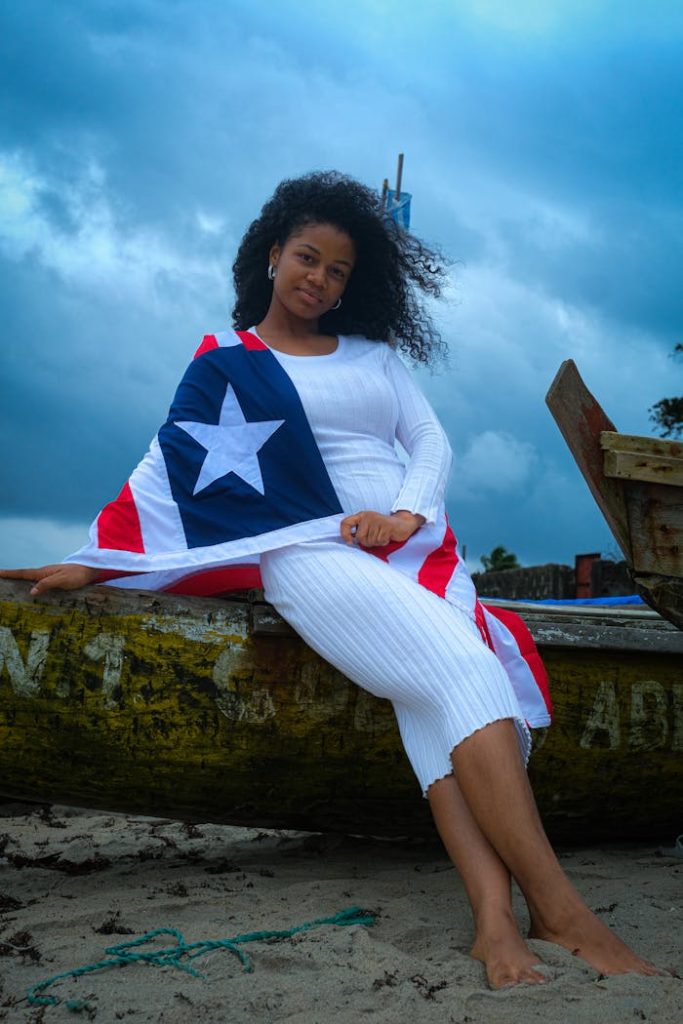 A woman draped in the Liberian flag sitting on a boat at the beach.