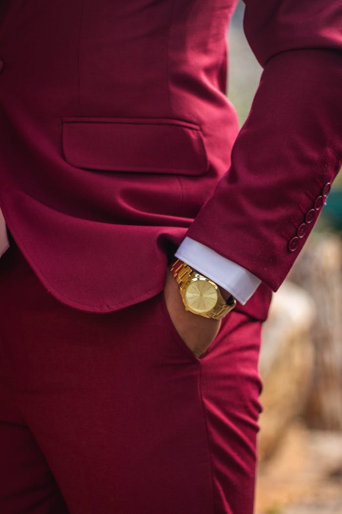 Close-up of a man in a burgundy suit showcasing a stylish gold wristwatch, perfect for formal elegance.