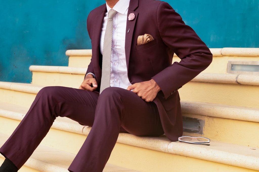 Elegant man in a burgundy suit sitting on steps, exuding sophistication and style.